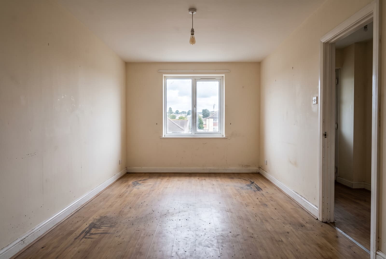Empty Devon rental room before an end-of-tenancy clean, scuffed flooring and marked walls under flat grey light